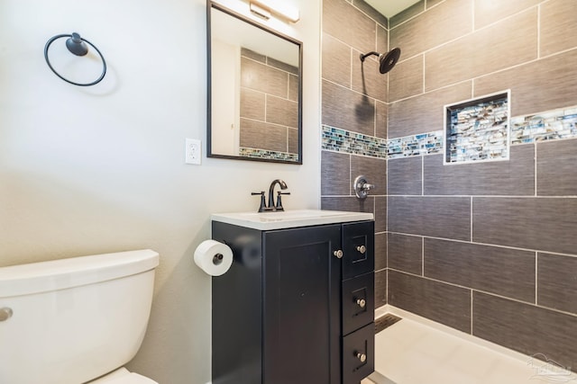 bathroom featuring tiled shower, toilet, and vanity