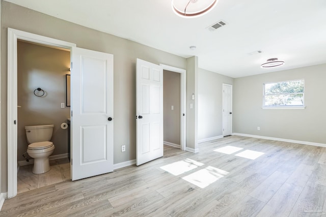unfurnished bedroom featuring light wood-style floors, ensuite bathroom, and baseboards
