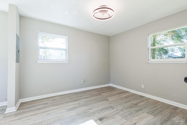 spare room featuring light wood finished floors, baseboards, and electric panel