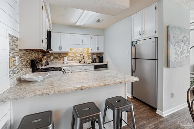 kitchen with a sink, dark wood-style floors, appliances with stainless steel finishes, a peninsula, and white cabinets