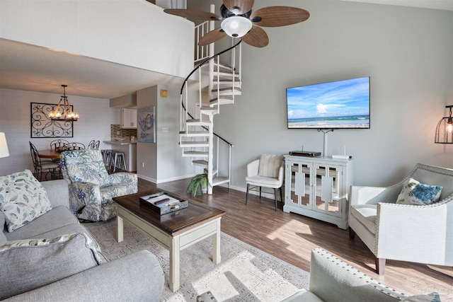 living room with ceiling fan with notable chandelier, wood finished floors, stairway, baseboards, and a towering ceiling