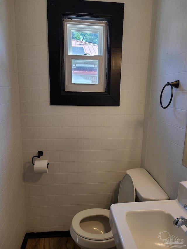 bathroom with toilet, sink, and tile walls