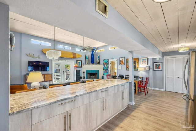 1112 Maldonado Dr, Pensacola Beach, FL 32561 - kitchen with hanging light fixtures, a brick fireplace, light stone countertops, light hardwood / wood-style floors, and stainless steel refrigerator