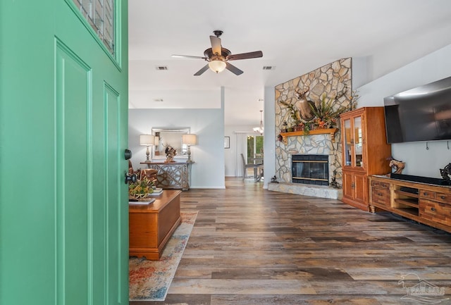living area featuring a ceiling fan, a stone fireplace, wood finished floors, and visible vents