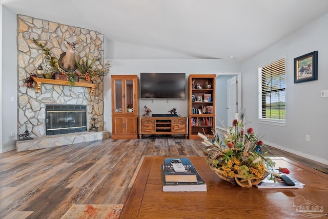living area featuring baseboards, vaulted ceiling, wood finished floors, and a fireplace