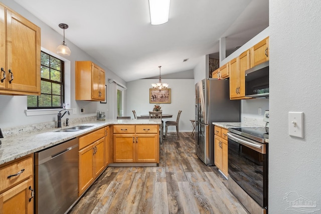 kitchen with a peninsula, wood finished floors, stainless steel appliances, a sink, and vaulted ceiling