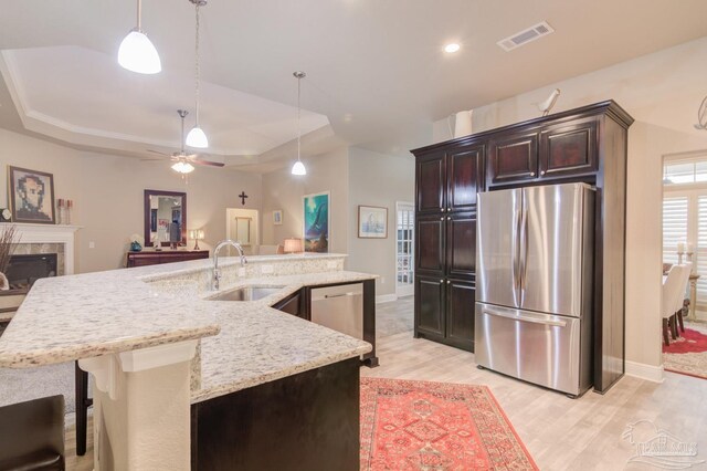 kitchen with sink, appliances with stainless steel finishes, hanging light fixtures, dark brown cabinetry, and light wood-type flooring