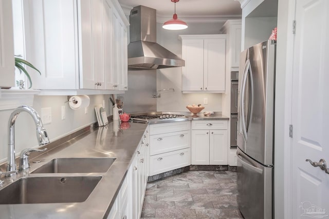 kitchen with wall chimney range hood, hanging light fixtures, stainless steel appliances, sink, and white cabinets