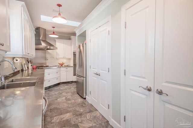 kitchen with wall chimney range hood, white cabinetry, hanging light fixtures, and stainless steel counters