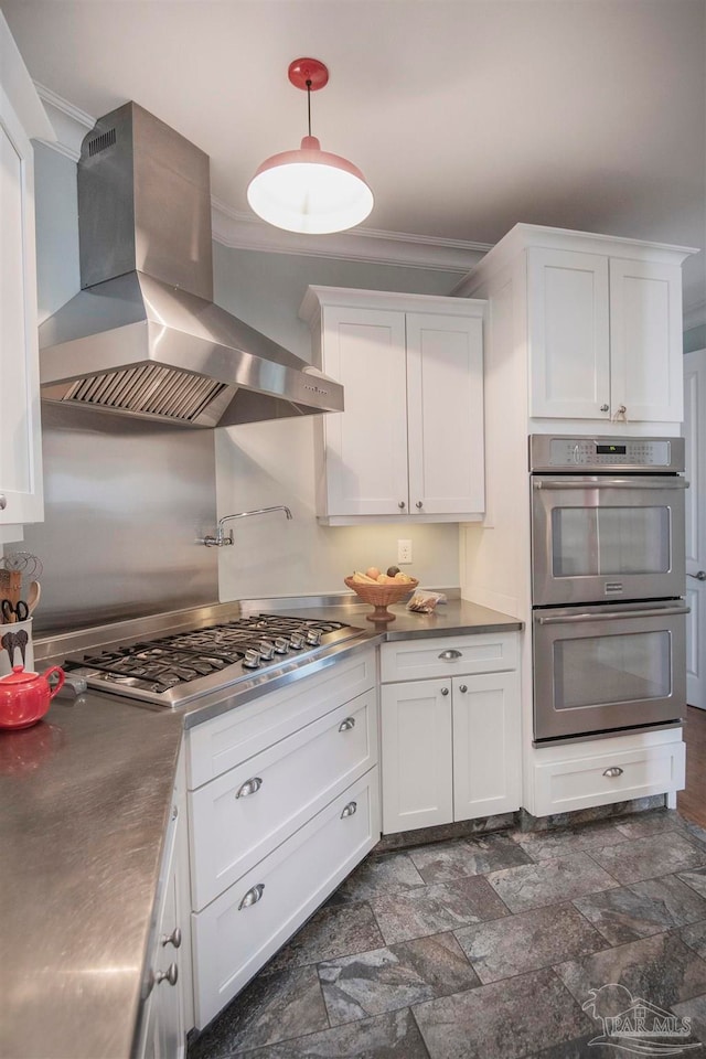 kitchen with appliances with stainless steel finishes, white cabinetry, and wall chimney range hood