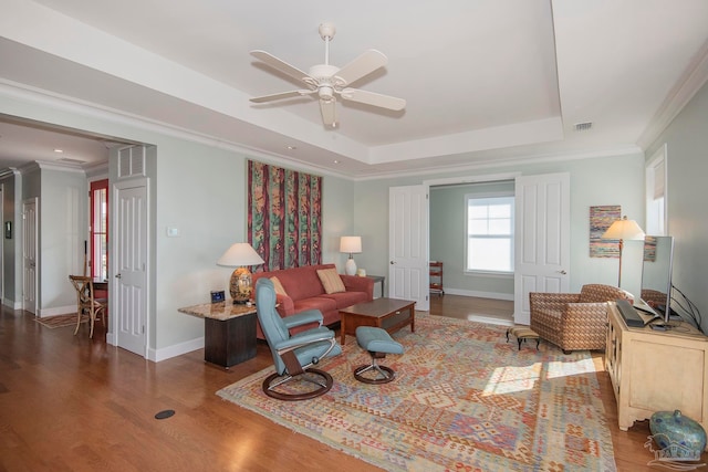 living room with ornamental molding, hardwood / wood-style floors, a tray ceiling, and ceiling fan