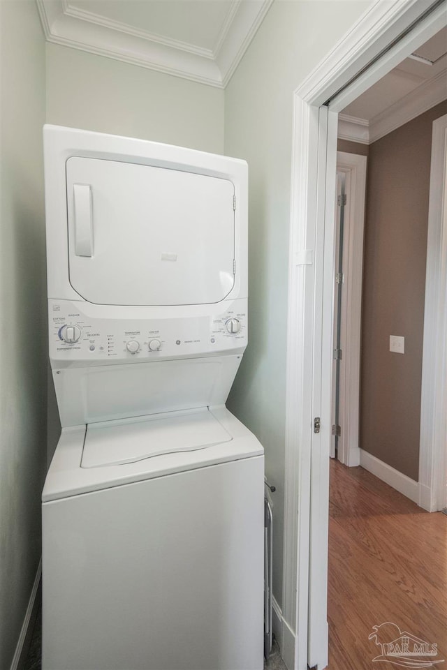 washroom featuring ornamental molding, stacked washing maching and dryer, and hardwood / wood-style flooring