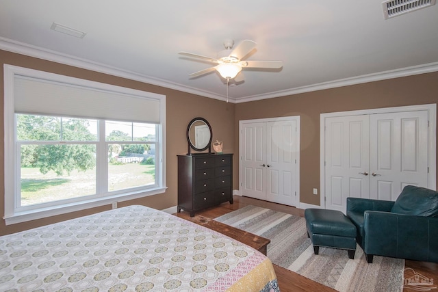 bedroom featuring ornamental molding, multiple closets, wood-type flooring, and ceiling fan