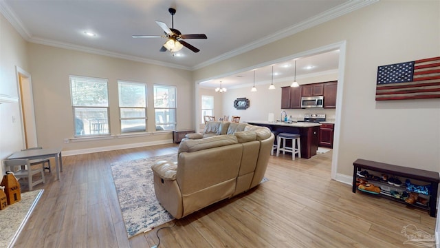 living room featuring ceiling fan with notable chandelier, sink, light wood-type flooring, and crown molding