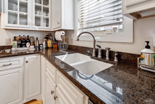 kitchen featuring dark stone counters, white cabinetry, and sink