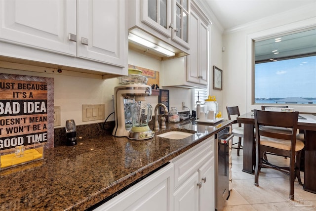 kitchen featuring light tile patterned flooring, sink, white cabinetry, crown molding, and dark stone countertops