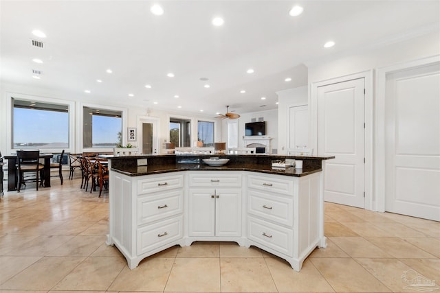 kitchen with dark stone counters, white cabinetry, ceiling fan, and a kitchen island