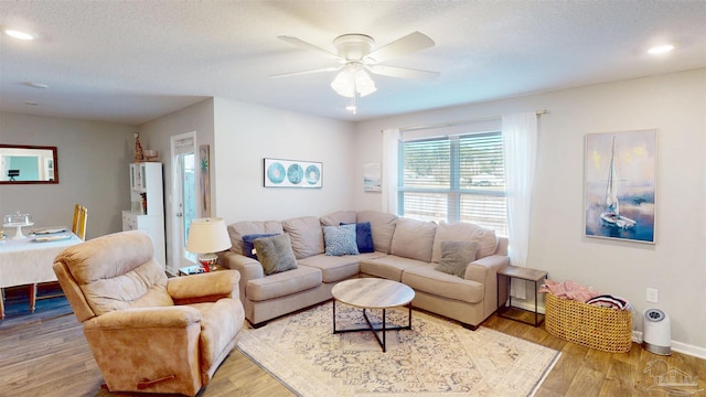 living room with a ceiling fan, light wood-type flooring, a textured ceiling, and baseboards