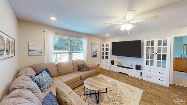 living area with ceiling fan, a textured ceiling, and wood finished floors