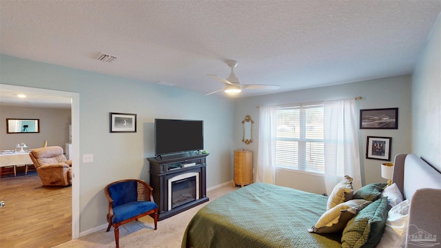 bedroom featuring visible vents, a glass covered fireplace, ceiling fan, a textured ceiling, and baseboards