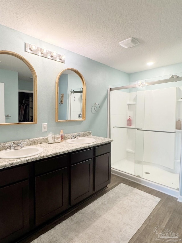 full bathroom with a textured ceiling, wood finished floors, a sink, and a shower stall