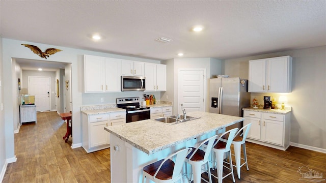 kitchen with a breakfast bar, white cabinetry, light countertops, appliances with stainless steel finishes, and an island with sink