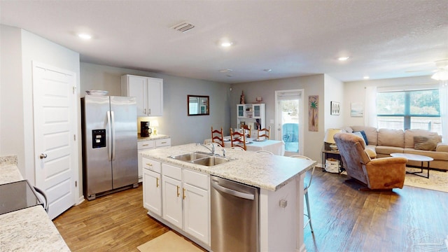 kitchen featuring a sink, white cabinets, open floor plan, appliances with stainless steel finishes, and an island with sink