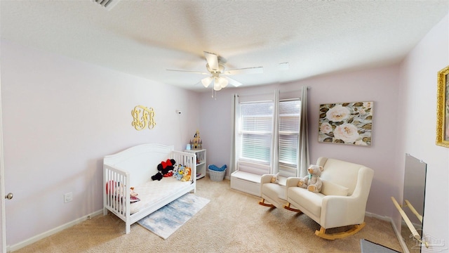 bedroom featuring a crib, light carpet, baseboards, a ceiling fan, and a textured ceiling