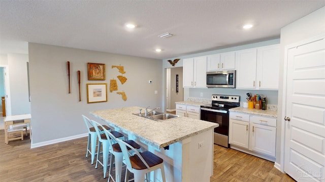 kitchen with stainless steel appliances, white cabinetry, a sink, and a center island with sink