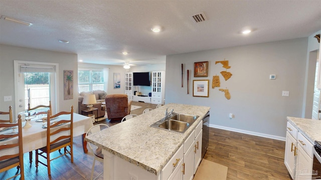 kitchen with a center island with sink, visible vents, open floor plan, white cabinets, and a sink