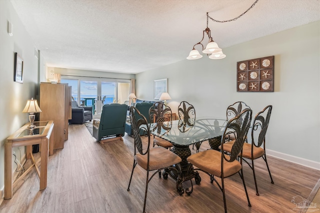 dining space with baseboards, a textured ceiling, an inviting chandelier, and wood finished floors