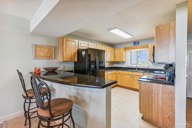 kitchen with a breakfast bar, a peninsula, light tile patterned flooring, a sink, and black fridge