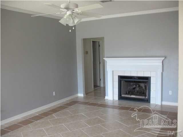 unfurnished living room featuring a tiled fireplace, crown molding, and ceiling fan