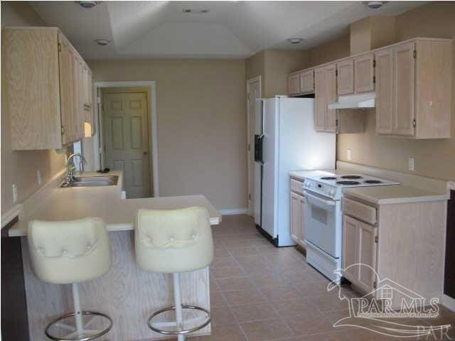 kitchen featuring sink, a kitchen breakfast bar, kitchen peninsula, lofted ceiling, and white appliances