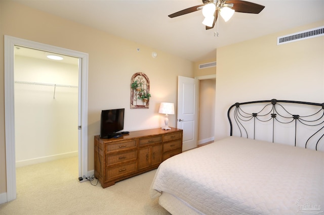 bedroom with ceiling fan, a walk in closet, light carpet, and a closet