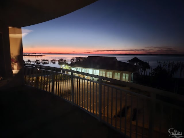 balcony at dusk featuring a water view