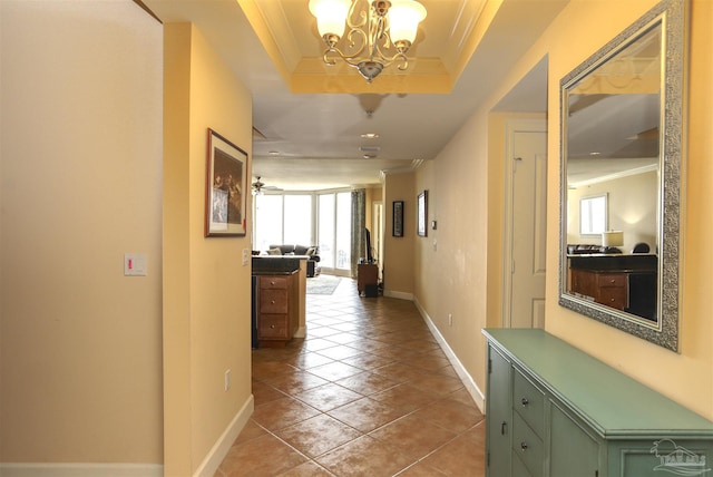 corridor featuring a chandelier, tile patterned flooring, a tray ceiling, and ornamental molding