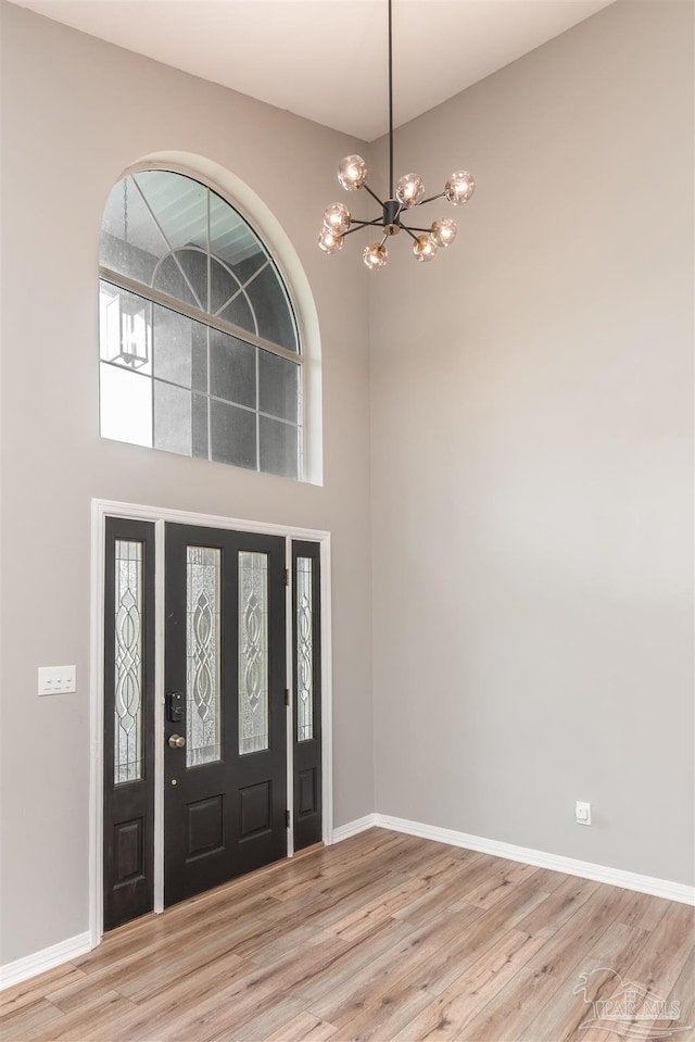 entryway featuring a towering ceiling, a chandelier, and light wood-type flooring