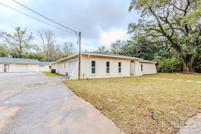 ranch-style home featuring aphalt driveway, central AC, a front yard, stucco siding, and an attached garage