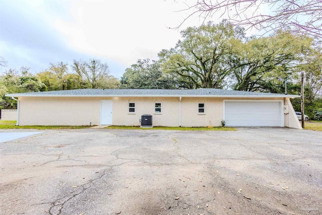 exterior space with a garage, driveway, central AC, and stucco siding