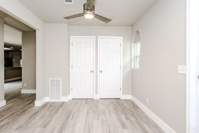 unfurnished bedroom featuring light wood finished floors, visible vents, arched walkways, and baseboards