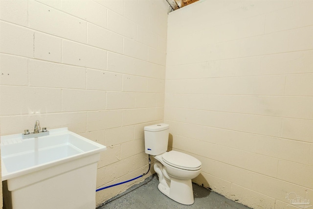 half bathroom featuring concrete block wall, toilet, unfinished concrete flooring, and a sink