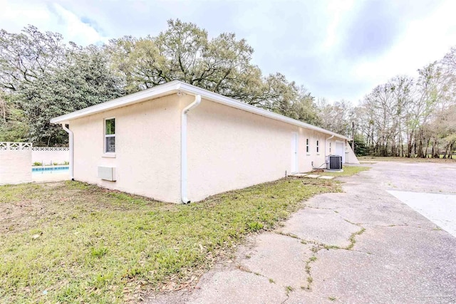 view of property exterior featuring a fenced in pool, fence, aphalt driveway, central AC unit, and stucco siding