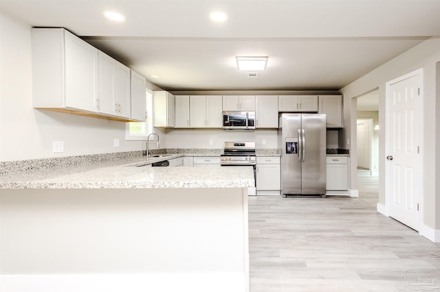 kitchen with light stone counters, appliances with stainless steel finishes, a peninsula, light wood-style floors, and a sink