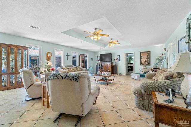 tiled living room featuring a textured ceiling, a tray ceiling, and ceiling fan