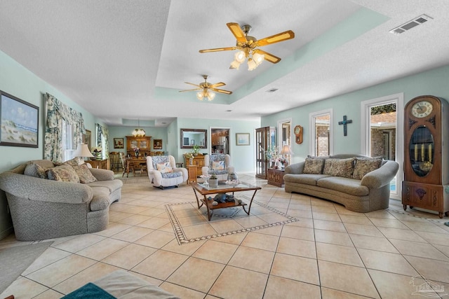 tiled living room with ceiling fan, a textured ceiling, and a tray ceiling