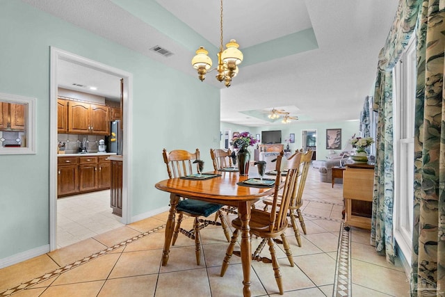 tiled dining space with a textured ceiling, a tray ceiling, and ceiling fan with notable chandelier