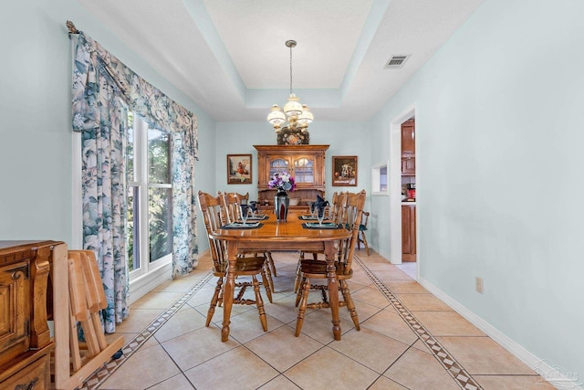 tiled dining room featuring a tray ceiling, plenty of natural light, and an inviting chandelier