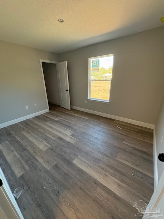 unfurnished bedroom with a textured ceiling, baseboards, and wood finished floors