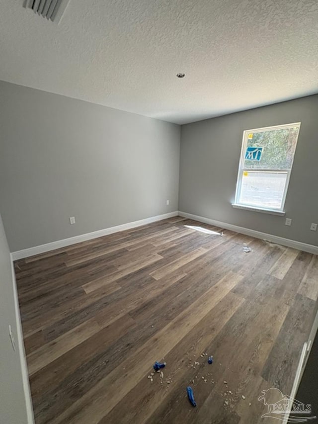 empty room with visible vents, a textured ceiling, baseboards, and wood finished floors